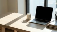 Modern workspace with laptop computer and coffee mug on wooden desk near window with natural sunlight for remote work and productivity.