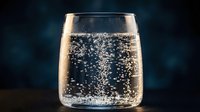 Sparkling water in a clear glass with rising bubbles on a dark blue background, refreshing drink concept.