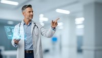 Middle-aged Caucasian male doctor in white coat pointing while holding digital tablet in modern hospital corridor with medical technology interface.