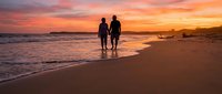 Romantic couple silhouettes walking on beach at sunset with golden sky and ocean waves creating peaceful vacation moment for travel and love themes.