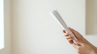 Woman with red nail polish holding stack of blank white papers against neutral background for business, office, or document-related projects.