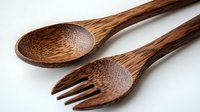 Rustic wooden spoon and fork utensils made from natural oak wood featuring rich brown tones and detailed grain texture on white background, eco-friendly kitchen accessories.