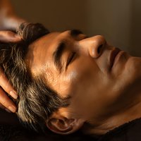 Mature Caucasian man receiving relaxing head massage therapy at spa with warm lighting for wellness and stress relief treatment.