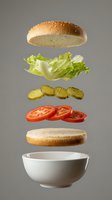 Deconstructed burger with floating sesame bun, lettuce, pickles, tomato slices and bowl on gray background for food service marketing.