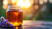 Golden honey jar glowing in sunset light with fresh lavender flowers on rustic wooden surface, soft bokeh background creates warm atmospheric mood.