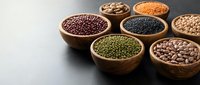 Assorted legumes and pulses in wooden bowls including lentils, beans, and chickpeas arranged on dark surface for healthy cooking and nutrition concepts.