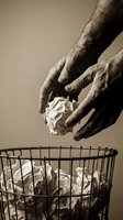 Elderly hands disposing crumpled paper ball into wire waste basket in sepia tone for environmental awareness and recycling concepts.