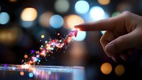 Magical sparkles trail from finger touch on glass surface with colorful bokeh background creating ethereal light path effect in dark atmospheric setting.