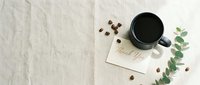 Black coffee mug with thank you card, coffee beans, and eucalyptus on linen background, flat lay top view with copy space.