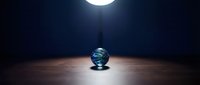 Crystal globe illuminated by overhead street lamp on dark asphalt surface at night, symbolizing global business, international commerce, and worldwide connectivity for corporate presentations.