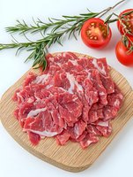 Fresh sliced raw beef on wooden cutting board with cherry tomatoes and rosemary sprigs, bright food photography on white background.