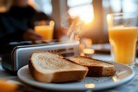 Toasted bread slices on white plate with orange juice glass and morning sunlight streaming through window, creating cozy breakfast atmosphere with steam rising.
