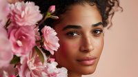 Young African American woman with natural curly hair and pink carnation flowers against soft pink background for beauty and skincare campaigns.