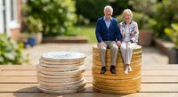 Happy senior couple sitting on stack of golden coins representing retirement savings and financial security planning for elderly lifestyle.
