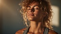 Young woman with curly hair enjoying sunlight with eyes closed, wearing tank top in warm golden hour glow. Peaceful moment of mindfulness.