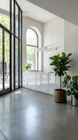 Modern minimalist kitchen interior with marble backsplash, black steel windows, concrete floors and potted plants creating bright contemporary living space.