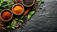 Aromatic spices in wooden bowls with turmeric, paprika powder, black peppercorns, fresh basil leaves, cinnamon sticks on dark stone background with copy space.