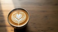 Cappuccino with heart latte art in ceramic cup on wooden table, overhead view of coffee drink with milk foam design for cafe menu and beverage marketing.