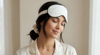 Young woman wearing white sleep mask with closed eyes in peaceful relaxation pose. Comfortable sleepwear and serene expression for wellness and rest concepts.