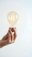 Hand holding glowing vintage Edison light bulb against white background symbolizing creativity innovation and bright ideas for business concepts.