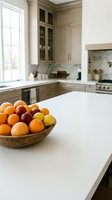 Fresh citrus fruits in wooden bowl on white kitchen counter with modern cabinetry, marble backsplash, and stainless steel appliances for home decor and lifestyle use.