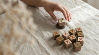 Hand arranging wooden alphabet blocks on textured surface for educational play and learning activities in natural lighting.