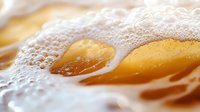 Extreme close up of light golden beer with white foam bubbles and froth in macro photography showing refreshing beverage texture and carbonation details.