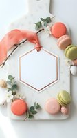 Elegant marble cutting board with colorful macarons, eucalyptus leaves, white flowers and coral ribbon arranged around hexagonal copper frame for spring styling.