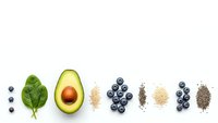 Healthy superfood ingredients arranged in row including spinach leaf, avocado half, blueberries, chia seeds and quinoa on white background.