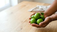 Hands holding fresh green limes on wooden table surface, suitable for food, cooking, recipe, and healthy lifestyle content.