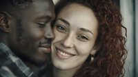 Happy interracial couple embracing intimately, young African American man and mixed race woman with curly hair smiling together in romantic moment for relationship content.