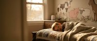 Young child peacefully sleeping in cozy bedroom with warm sunlight streaming through window and farm animal wall decals creating nurturing atmosphere.