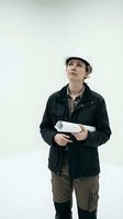 Female construction worker or architect wearing white hard hat and black jacket, holding rolled blueprints while looking upward, isolated on white background for design projects.