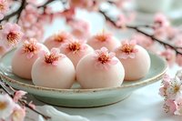 Pink cherry blossom mochi desserts on ceramic plate surrounded by sakura flowers for spring celebration and Japanese cuisine presentation.