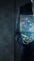 Businessman in dark suit holding holographic display showing cityscape with financial data, charts, and glowing green analytics overlay for technology and business concepts.