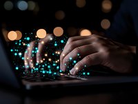 Hands typing on laptop keyboard with glowing turquoise digital particles and bokeh lights emerging, representing technology innovation and digital transformation.