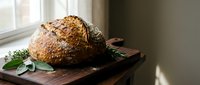 Freshly baked artisan bread loaf with seeds on rustic wooden cutting board near window. Homemade sourdough with natural lighting for bakery and food concepts.