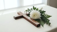 Wooden cross with white chrysanthemum flower and green foliage on white surface for memorial, funeral, religious ceremony or spiritual remembrance concept.