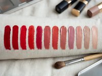 Lipstick color swatches on arm showing red to nude gradient palette with makeup brushes for beauty testing and cosmetic product selection.