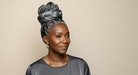 Mature African American woman with gray braided updo hairstyle wearing dark gray t-shirt against neutral beige background. Portrait suitable for diversity, aging, fashion and lifestyle content.