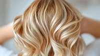 Blonde wavy hair with balayage highlights and soft curls styled in modern beach waves showing professional hairdressing technique and trendy hair color result.