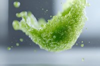 Fresh green celery slice splashing through water with droplets and bubbles creating dynamic motion against gray background. Suitable for healthy lifestyle content.