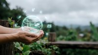 Hands holding glowing digital globe with network connections over green natural landscape representing global connectivity and environmental technology solutions.