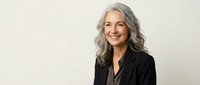 Confident mature businesswoman with silver gray hair smiling warmly in professional black blazer against neutral background for corporate marketing.