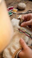 Close-up of hands working on traditional embroidery with colorful threads on linen fabric, crafting and needlework hobby at wooden table with supplies.