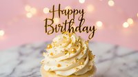 Elegant birthday cupcake with golden Happy Birthday topper, cream frosting, gold sprinkles, bokeh lights, pink background, marble surface.