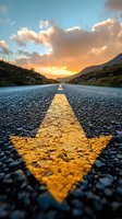 Empty asphalt road with yellow arrow marking leading through mountain valley at golden sunset with dramatic clouds for travel and journey concepts.