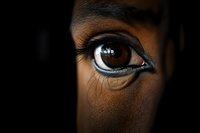 Close-up macro shot of dark brown eye with dramatic black eyeliner and mascara against deep black background, showing intricate details of iris and eyelashes.