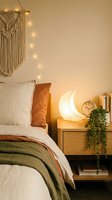 Cozy boho bedroom interior with macrame wall hanging, fairy lights, moon lamp and trailing plant on wooden nightstand creating warm ambient atmosphere.