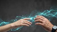 Two hands reaching toward each other with glowing blue digital energy waves and particles flowing between them on dark background for technology concepts.
